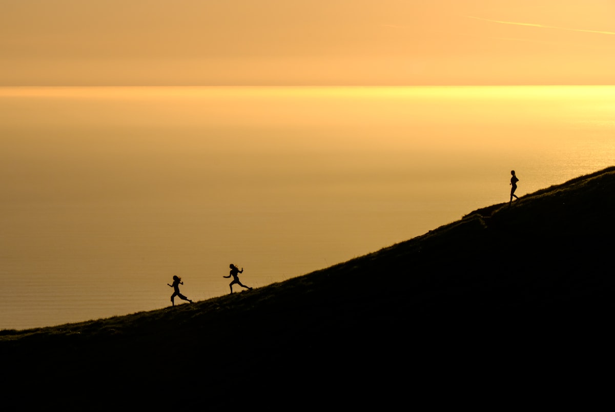 Runners ascending a hillside silhouetted against a golden ocean sunset